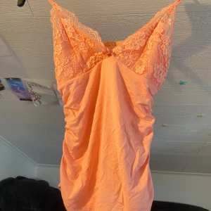 Persikofärgad linnetopp med spets från SHEIN - Säljer en persikofärgad linnetopp från SHEIN med vackra spetsdetaljer upptill och smala axelband. Toppen är ärmlös och har en mjuk, stretchig känsla. Perfekt för varma dagar eller som lager under en kofta. Har bara provat en gång men aldrig haft ute.