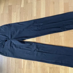 Svarta kostymbyxor från Lindex - Snygga svarta kostymbyxor från Lindex i klassisk rak modell. Byxorna har pressveck och normal passform, perfekta för en stilren look. Passar dig som vill ha en enkel och tidlös byxa.