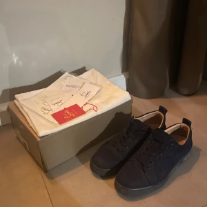 Christian Louboutin pris kan diskuteras  - Säljer ett par mörkblå sneakers från Christian Louboutin i mocka med den ikoniska röda sulan. Skorna har rund tå och platt sula, samt diskret broderad logga på sidan. Kommer med originalkartong, dustbag och äkthetsbevis.