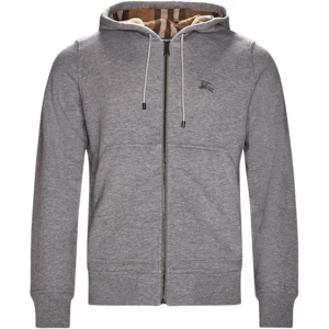 Grå hoodie med dragkedja från Burberry - Säljer en stilren grå hoodie från Burberry med dragkedja och justerbar huva. Insidan av huvan har det klassiska Burberry-rutiga mönstret. Tröjan har långa ärmar och diskret logga på bröstet.