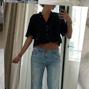 Svart broderad blus från Zara - Säljer en svart croppad blus från Zara med broderade detaljer och korta ärmar. Blusen har v-ringning och knappar framtill. Storlek S.