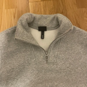 Grå halvzip sweatshirt - Säljer en grå sweatshirt från H&M med halv dragkedja och hög krage. Tröjan har långa ärmar och ribbade muddar vid ärmslut och nederkant. Perfekt för en avslappnad och stilren look.