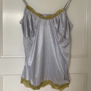 Silvrig linnetopp med spetsdetaljer - Silvrig linnetopp med tunna axelband och dekorativa gröna spetsdetaljer längs halsringning och nederkant. Köpt vintage i Sydney. 