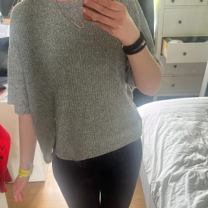 Grå ribbad oversized tröja - Säljer en grå ribbad tröja med oversized passform och korta ärmar. Tröjan har en rund halsringning och är tillverkad i ett mjukt, stickat material som känns skönt mot huden. Perfekt för en avslappnad och stilren look.