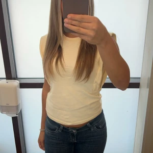 Vit t-shirt med axelvaddar - Säljer en stilren vit t-shirt med markerade axlar och rund halsringning. T-shirten har en rak passform och är perfekt att matcha med jeans eller kjol.