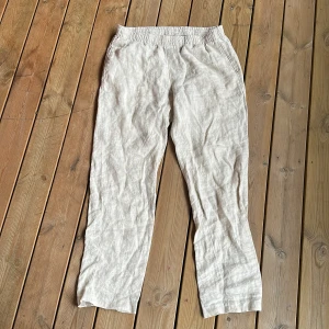 Beige linnebyxor från H&M - Säljer ett par ljusbeige linnebyxor från H&M med snörning i midjan. Byxorna har raka ben och är tillverkade i ett luftigt linnematerial, perfekta för varmare dagar.