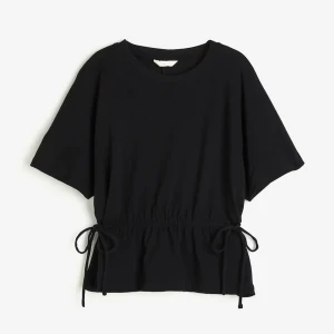Trendig hm topp med knyt i midjan - Svart t-shirt från H&M med korta ärmar och rund halsringning. Toppen har knytband i midjan som ger en snygg passform och en enkel, stilren look. Aldrig använd.