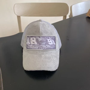 Ljusgrå keps från Von Axelsson (DIF) - Säljer en ljusgrå keps från Von Axelsson med mesh på sidorna och baksidan. Framsidan har en stor patch med tryck i vitt och grått med Djurgården. Kepsen har böjd skärm och justerbar passform. Denna keps är sällsynt då den ej säljs längre.