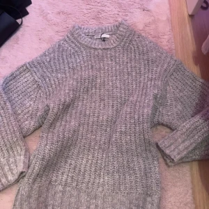 Grå stickad tröja från Pull&Bear - Mysig grå stickad tröja från Pull&Bear med grovstickat mönster och rund halsringning. Perfekt för kyliga dagar och enkel att matcha med olika outfits.