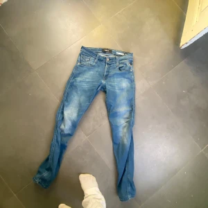 Blå Replay jeansbyxor - Säljer ett par klassiska blå jeans från Replay med fem fickor och snygga slitningar. Byxorna har normal passform och raka ben. Perfekta för dig som gillar en tidlös jeanslook.