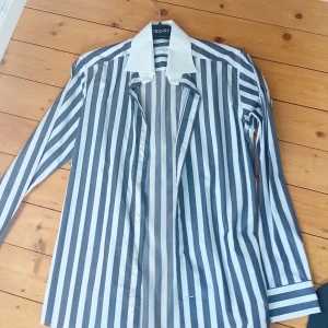 Randig skjorta från Eton med vit krage - Snygg skjorta från Eton med breda grå och vita ränder samt kontrasterande vit krage. Klassisk passform med långa ärmar och knappar framtill. Perfekt för dig som vill sticka ut lite extra.