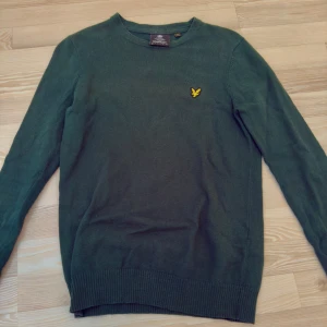 Grön Stickad Lyle & Scott - Mörkgrön långärmad tröja från Lyle & Scott med rund halsringning och den klassiska gula loggan broderad på bröstet. Tröjan är i bomull och ull och har ribbade muddar vid ärmslut och nederkant. XS i storlek men sitter som S. Nypris: ca. 800