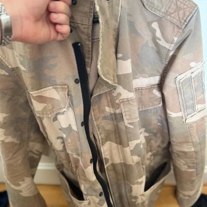Camouflage field jacka från Zadig & Voltaire - Säljer en snygg camouflagefärgad jacka från Zadig & Voltaire. Jackan har flera fickor framtill, dragkedja och knappar samt en patch på ena ärmen. 