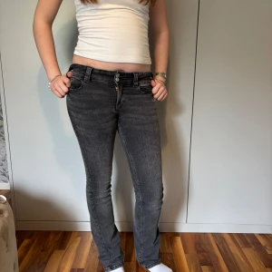 Grå bootcut jeans från H&M - Säljer ett par grå bootcut jeans från H&M med låg midja. Jeansen har klassisk femficksdesign, knappar och dragkedja framtill samt justerbar midja. Perfekta för dig som gillar en tidlös och enkel stil.