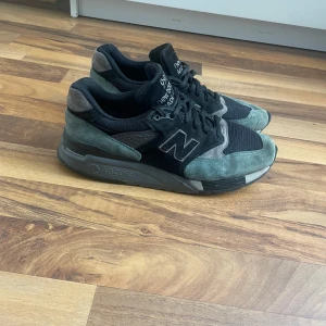 New Balance sneakers i svart och grå mocka - Säljer ett par New Balance sneakers i svart och grå mocka med klassisk N-logga på sidan. Skorna har platt sula och snörning, perfekt för en stilren vardagslook. Ny köpta för 6500. Ingen sula i skon!