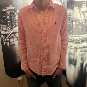 Rosa skjorta från Ralph Lauren - Säljer en klassisk rosa skjorta från Ralph Lauren med knappar framtill och broderad logga på bröstet. Skjortan har lång ärm och normal  passform, perfekt för en stilren look. Och är perfekt nu när sommaren närmar ☀️(original pris 1500kr  !!!)