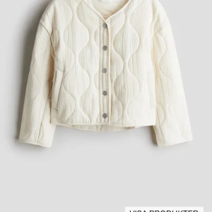 Quiltad beige jacka med tryckknappar - Säljer en beige quiltad jacka med vågigt mönster och tryckknappar framtill. Jackan har lång ärm, rund halsringning och är något croppad i modellen. Perfekt för lager-på-lager och enkel att styla till olika outfits. Storlek 164 från hm. Helt oanvänd med prislapp 