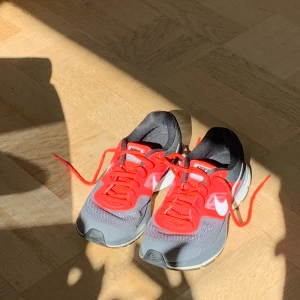 Nike Pegasus 30 löparskor med röd och grå färg - Nike Pegasus 30 sneakers i grått och rött med vita detaljer och röda snören. Skorna har en sportig design med meshmaterial för bra andningsförmåga och en bekväm platt sula. Perfekta för löpning eller träning.