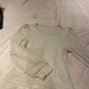  ribbad långärmad tröja - Säljer en vit ribbad tröja med rund halsringning och puffade axlar. Tröjan har långa ärmar med breda muddar och är i ett mjukt, stretchigt material. 