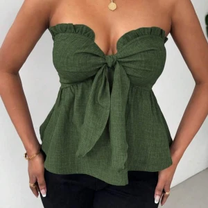 Grön axelbandslös topp med rosett - Säljer en snygg grön axelbandslös topp med volang och stor rosett framtill. Toppen har en lätt rynkad kant upptill och är perfekt för sommardagar. Passar till både jeans och kjol.
