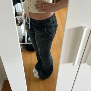 Mörkgrå bootcut jeans med slitningar - Säljer ett par svarta bootcut jeans med snygga slitningar och dubbla knappar i midjan. Sparsamt använda men är lite trasiga längst ner då dom är för långa för mig. Även därför jag säljer dom. Står ingen storlek men sitter som 26/27 i midjan och 32 i längd