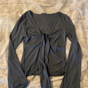 Svart långärmad topp - Svart långärmad topp ifrån Gina Tricot, storlek M. Aldrig använd, endast testad. Prislappen sitter kvar på. Knytning upptill och ”delning”. 