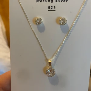 Smyckeset i silver med cubic zirconia - Säljer ett elegant smyckeset i sterling silver 925 med halsband och matchande örhängen. Både halsbandet och örhängena har runda hängen med gnistrande cubic zirconia-stenar. Kedjan är 42+3 cm lång.