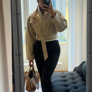 Beige croppad jacka med bälte - Säljer denna otroligt snygga sommar jackan!! Man kan justera den i hur tight man vill ha den runt midjan!! Säljer då den inte kommer till anvdäning, använd 1 gång från other stories, köptes förra sommaren, str 32/34, köptes för 999