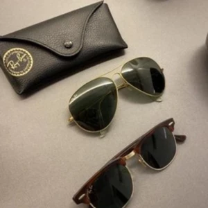 Ray-Ban solglasögon aviator och clubmaster - Två par Ray-Ban solglasögon: ett par klassiska aviator med guldfärgad metallbåge och mörkgröna glas, samt ett par clubmaster med brunsköldpaddsfärgad ovandel och gulddetaljer. Båda har svarta linser och Ray-Ban-logga på glaset. Fodral till ett par . 300 kr styck eller båda för 550 med fodral . 100 kr fodral 