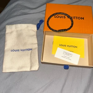 Louis Vuitton armband - Säljer ett exklusivt armband från Louis Vuitton i brunt med klassiskt monogrammönster och guldfärgat spänne. Kommer med original ask, tygpåse och äkthetskort. Perfekt accessoar för att lyfta din stil.