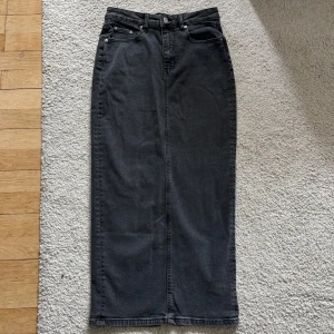 Mörkgrå jeanskjol med slits baktill  - Säljer en mörkgrå lång jeanskjol med slits baktill från Gina Tricot. Kjolen har 4 fickor, hög midja och en slits bak. Perfekt att styla med sneakers eller boots för en cool look.                                                                            Aldrig använd men utan prislapp. 