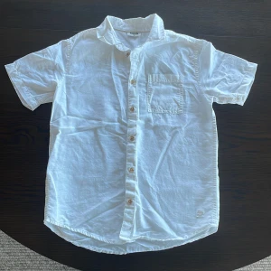 Vit kortärmad skjorta - Fräsch vit skjorta  från Kappahl med korta ärmar och bröstficka. Perfekt för varma dagar och enkel att matcha med jeans eller shorts. Knappar framtill och klassisk krage ger en clean look.