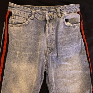 Jens med detalj! - Fina jeans med randig deltalj på sidan. Ränderna på sidan är i mörkblå och röd färg. Jeansen är i fint skick och i storlek M. Skulle säga att byxorna är i ”rak form”. Säljer pga att de inte kommer till användning☺️ 100kr+frakt
