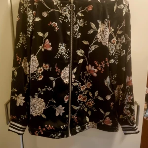 Jacka i satin och fina detaljer. - Snygg tunn jacka med blommor och glittriga muddar