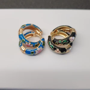 Örhängen stål  - Örhängen hoops i kirurgiskt stål med emaljerade blommor. Blåa eller svarta.hur läckra som helst men har knappt örsnibbar så dessa var större än jsg trodde vid beställningen därmed för tunga för mig. Enbart provade. Pris 90kr/styck eller 160kr för båda.