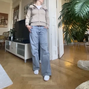 Stickad luvtröja  - Stickad tröja med luva, dragkedja och bruna detaljer. Perfekt nu till hösten och vintern då den är väldigt mysig och varm! Gjord i ullmaterial. 