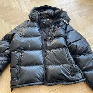 Nyinköpt  Polo Ralph Lauren Water-Repellent Down Jacket Färg: POLO BLACK GLOSSY Storlek: XL Ord pris 5495kr Säljs för 2000kr. Anv 4 ggr , p g a mindre olyckshändelse hål i vänster arm som lagats hos skräddare, se bild.