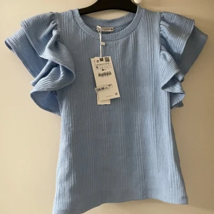 Ljusblå Topp med volanger - Ny och aldrig andvänd prislapp kvar. Normalpassform. 