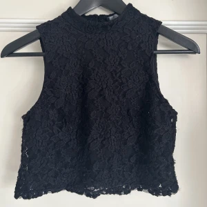 Crop top med spets  - Söt corp top med hög hals. Toppen är i två lager, ett tyg och ett spets. Knäppning i nacken. I använt skick.