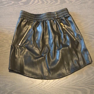 Fin Petit Sofie Schnoor svart fake skinnkjol  - En fin svart fake skinnkjol med guldigfärgade dragkedja. Endast använd en gång och i mycket fint skick. 