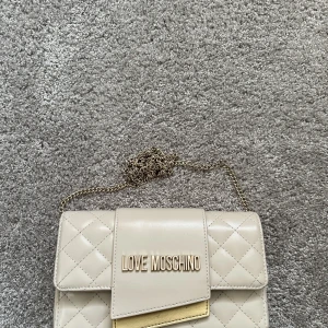 Love Moschino väska - Säljer nu min cremevita Love Moschino väska. Använd ett fåtal gånger. Skick 10/10. Medföljer dustbag till väskan. Pris är diskuterbart.
