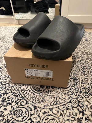 Yeezy slide  - Yeezy slides onyx i storlek 43. Använts Max 10 ggr därav lite nedtryckta och lite smuts på undersidan samt lite slitna längst fram. Skriv för fler bilder.  Köpta från CONFIRMED. Mitt pris 750 kr med hänsyn till slitaget, öppen för prisförslag snabb affär!