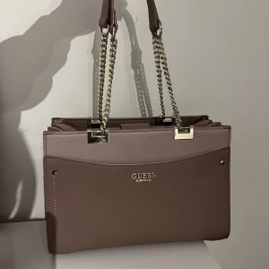 Guess väska - Rosa guess väska i superfint skick. Säljer då jag inte fått användning för den då jag mest använder totebags. Jättemånga fack osv! Skriv för fler bilder. Pris kan diskuteras vid snabb affär😊