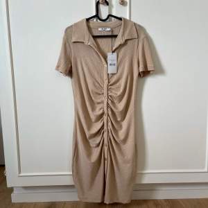 Beige/guld klänning med rysh från NA-KD. Nypris 499kr.  Aldrig använd med lappen kvar.