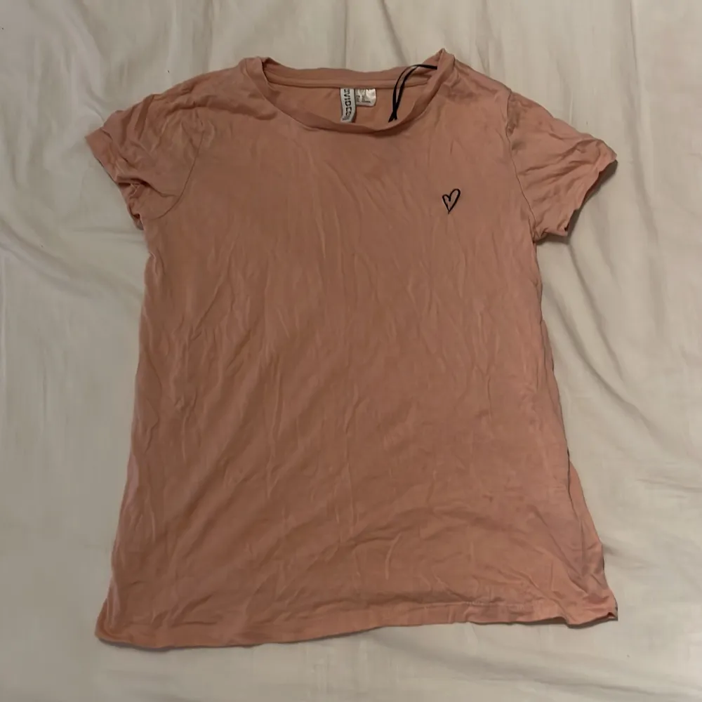 En rosa t shirt i storlek XS från H&M med ett litet hjärta in broderad. Väldigt stretchigt tyg. Tröjan ser lite beige ut i bilden men är egentligen ljus rosa. T-shirts.