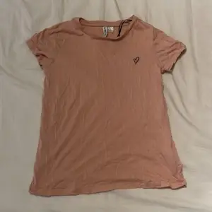 En rosa t shirt i storlek XS från H&M med ett litet hjärta in broderad. Väldigt stretchigt tyg. Tröjan ser lite beige ut i bilden men är egentligen ljus rosa