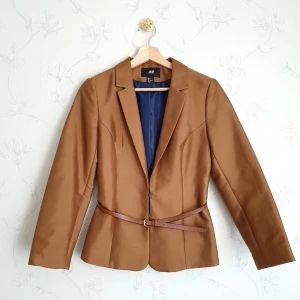 Brun kort kavaj - 🤎FÖRST TILL KVARN!🤎 Brun strukturerad kavaj i glanigt tyg. Skärpet i bilden kommer tillsammans med kavajen. Kavajen kan kläs upp eller ner beroende tillfälle, super elegant och preppy att ha med kjol eller dressade byxor. Vill bli av med ASAP!🤗