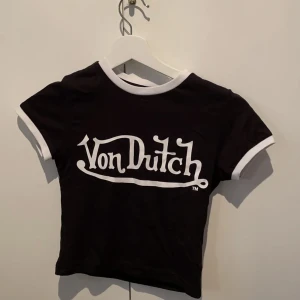 Croppad babytee | Von Dutch  - En super fin äkta svart-vit topp/babytee från Von Dutch med y2k vibe. Aldrig använd, endast testad. Därför är den i nytt skick. I storlek S. Säljer då den är lite för liten kring armarna. Lite mindre i storleken.