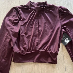 Vinröd topp  - Fin vinröd topp med öppning i mitten. Köpt på Nelly. Prislappen är kvar . Den är helt ny 