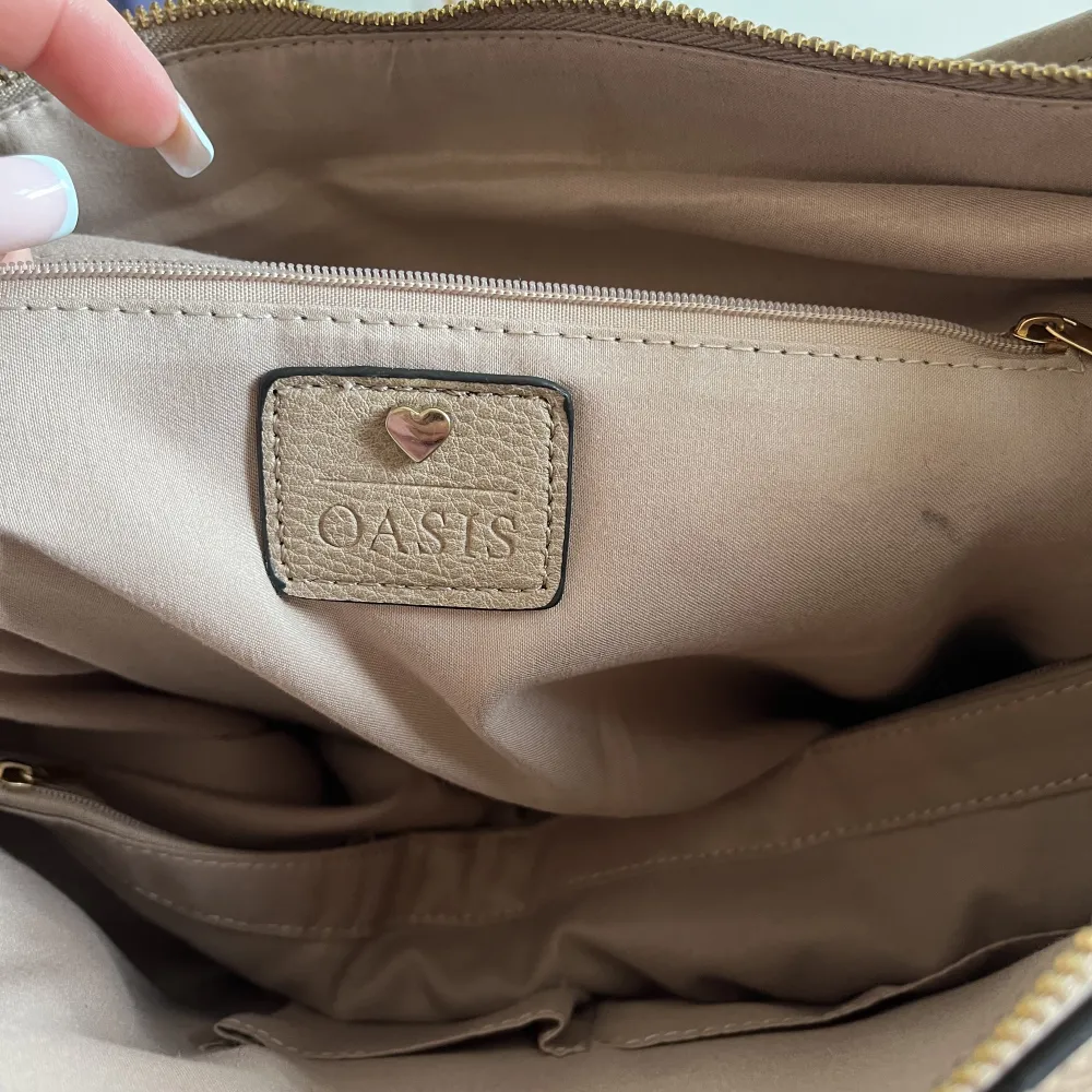 Superfräsch väska från märket Oasis (köpt på accent)! Rymlig med bra fickor och i en brun/beige färg. . Väskor.